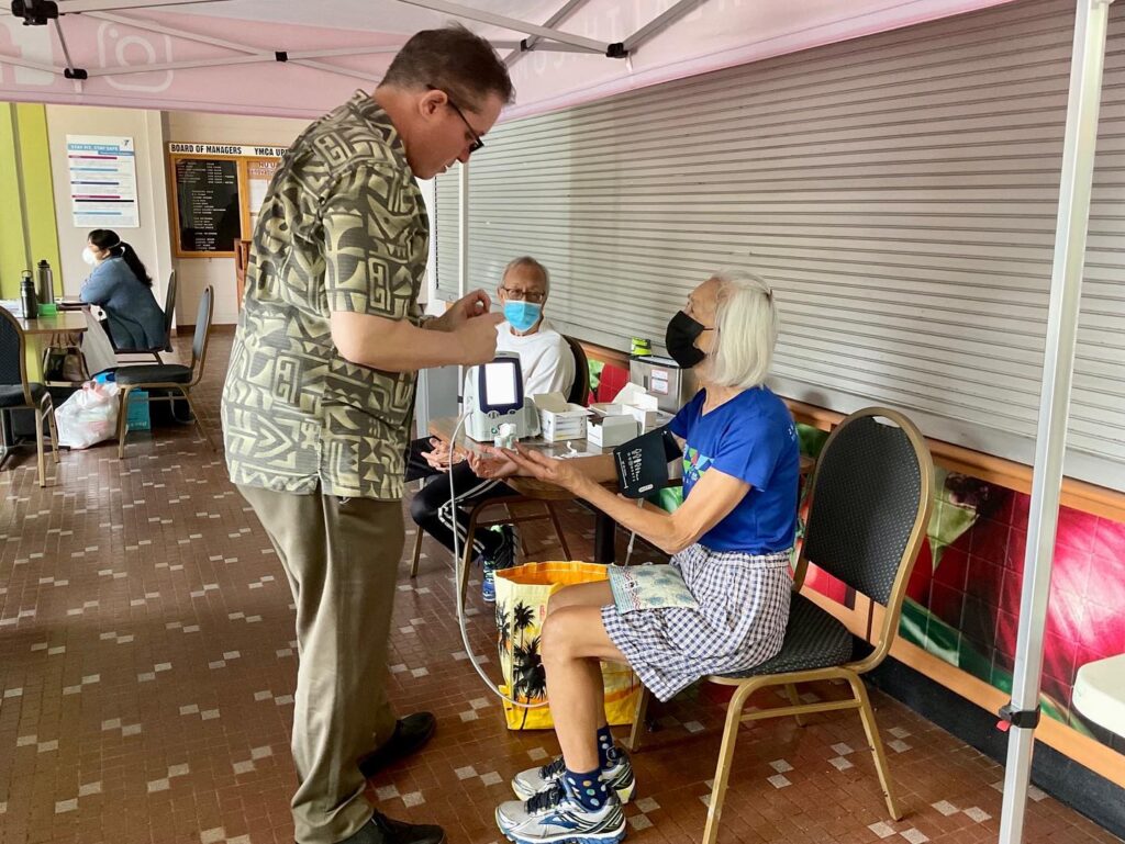 Healthcare worker checking an elderly woman’s blood pressure at a community event.